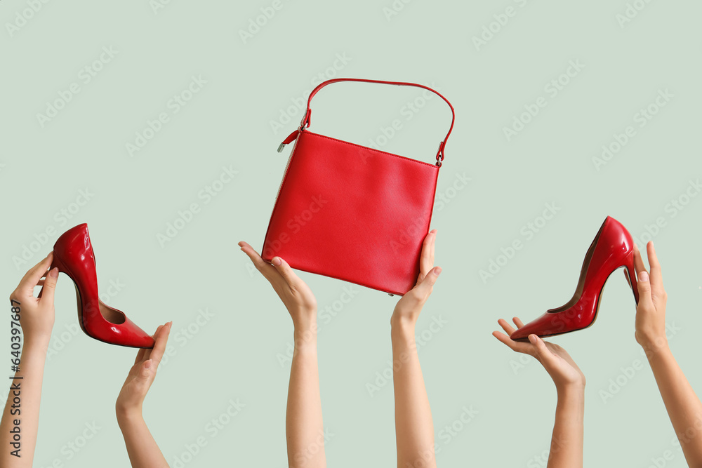 Female hands holding stylish bag and high heels on pale green background