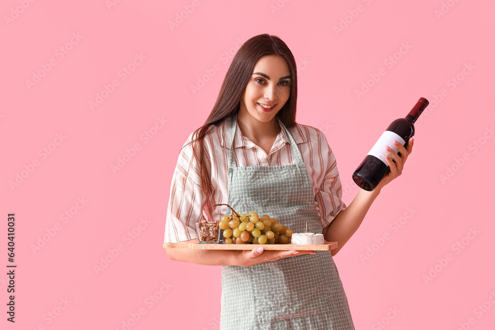 Young woman with bottle of wine and snacks on pink background