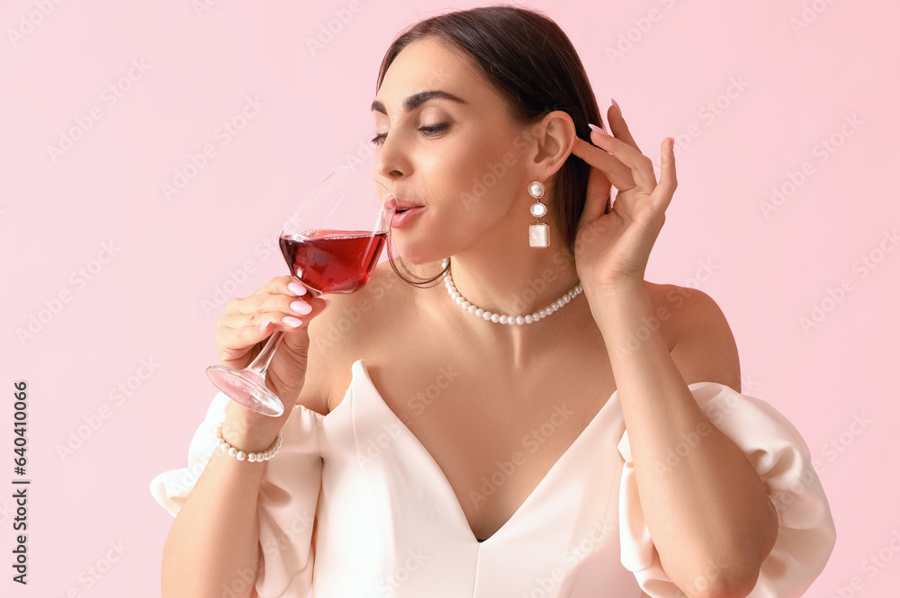 Young woman drinking wine on pink background, closeup