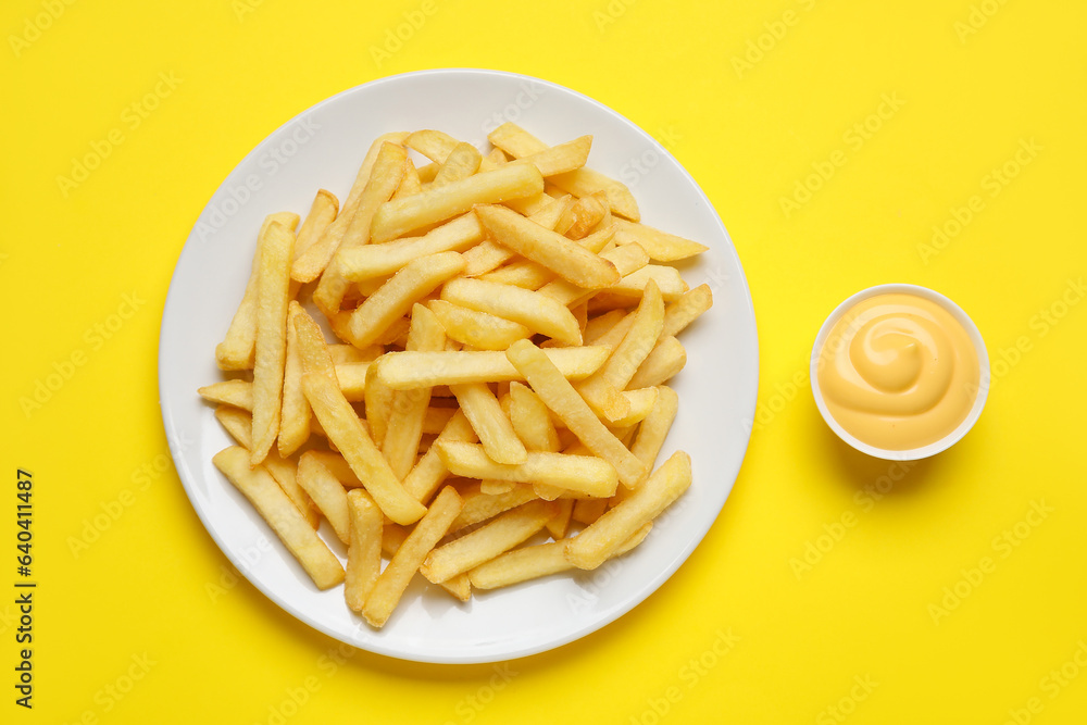 Plate with golden french fries and cheese sauce on yellow background