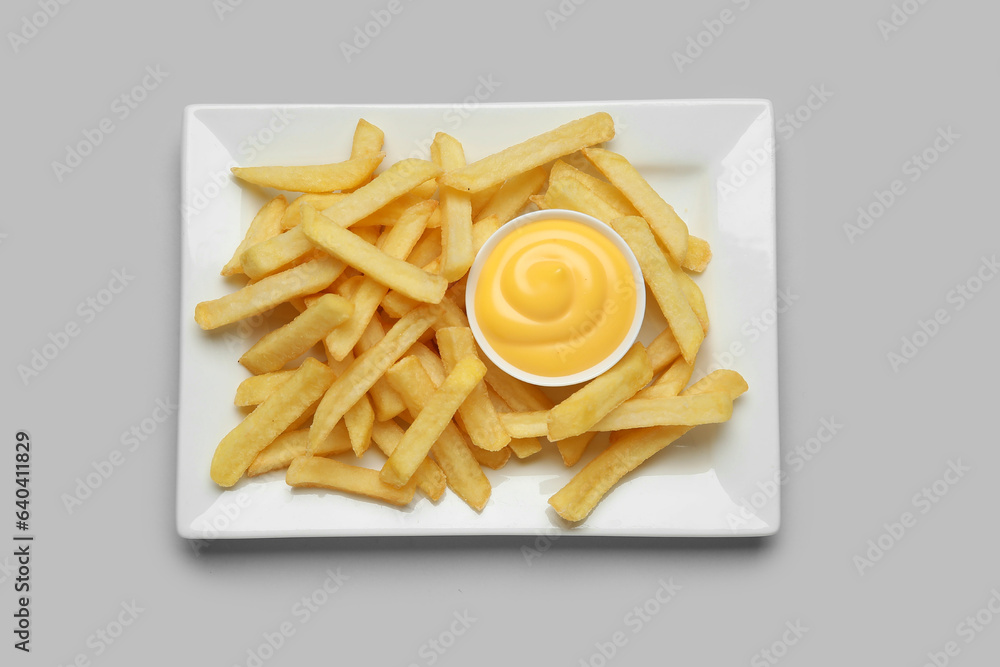 Plate with golden french fries and cheese sauce on grey background