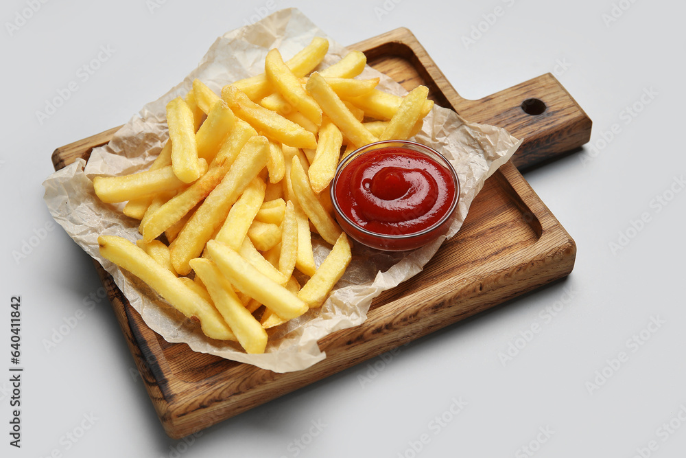 Wooden board with golden french fries and ketchup on grey background