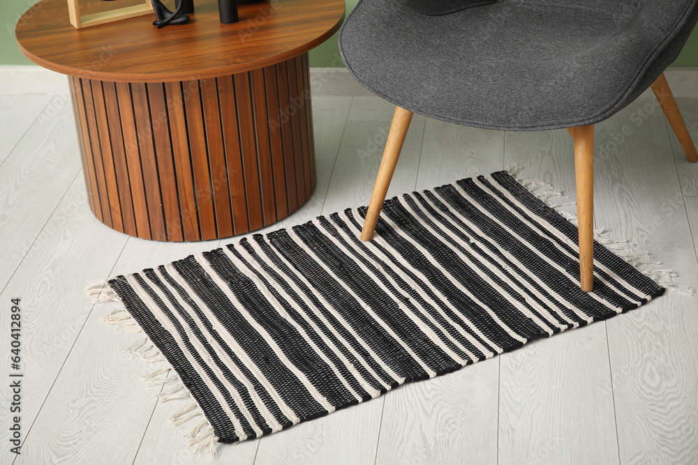 Stylish rug, grey armchair and coffee table near green wall