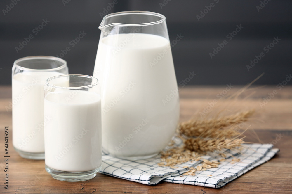 Glasses and jug of fresh milk with wheat ears on wooden table