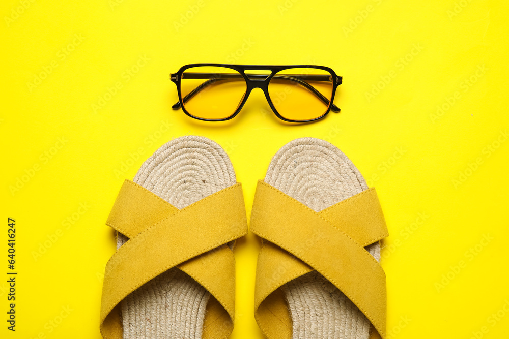 Stylish yellow sandals and sunglasses on color background