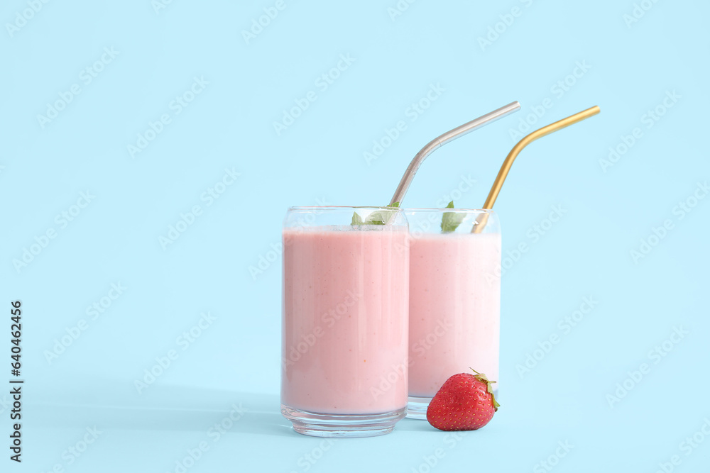 Glasses of tasty strawberry smoothie on blue background