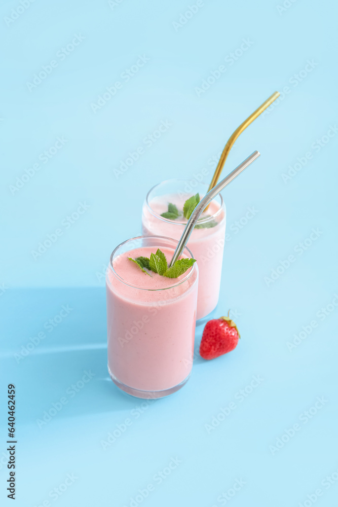 Glasses of tasty strawberry smoothie on blue background