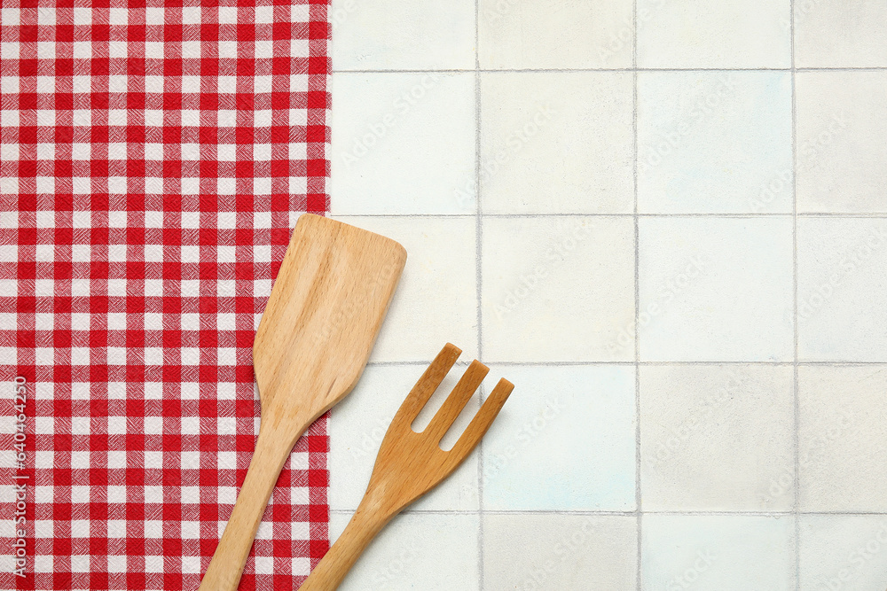 Wooden spatula, fork and napkin on white tile background