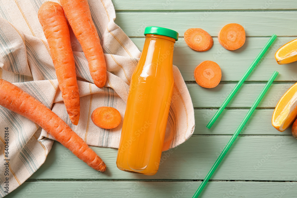 Bottle of fresh carrot juice with orange on green wooden background