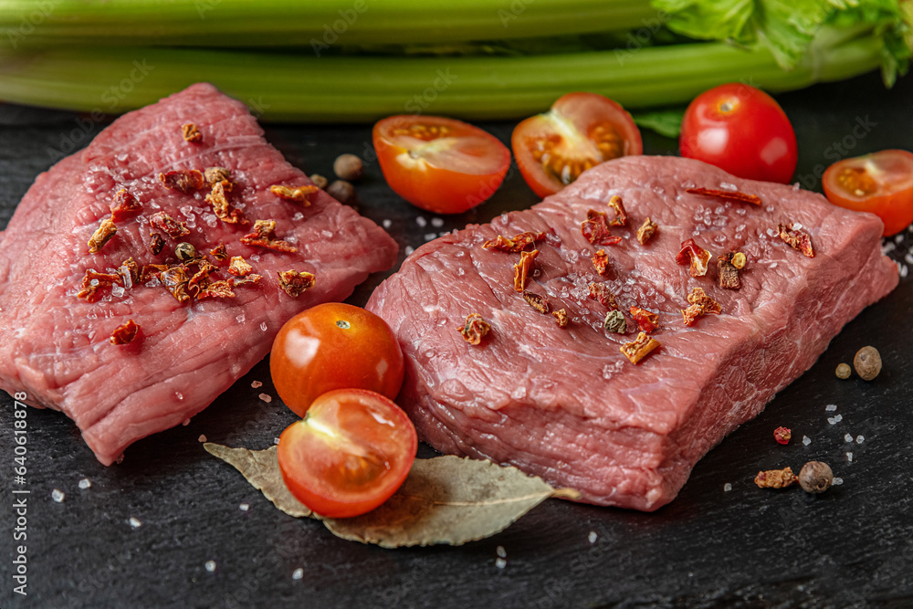 fresh raw meat with cherry tomatoes, spices and herbs on a black slate surface