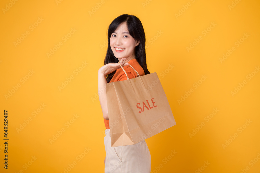 Trendy asian woman 30s in orange shirt celebrating a shopping spree with discounted purchases. Happy