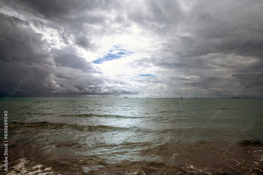 Beautiful dark evening sea and sky with dark clouds through which light passes.