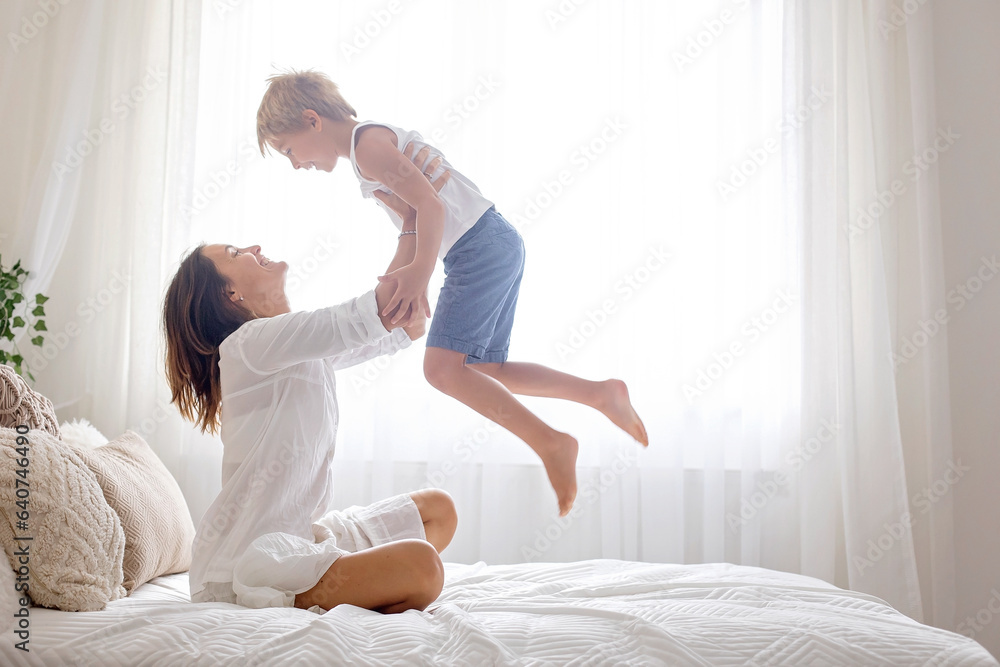 Mother, playing with her preschool child at home in bed, having fun