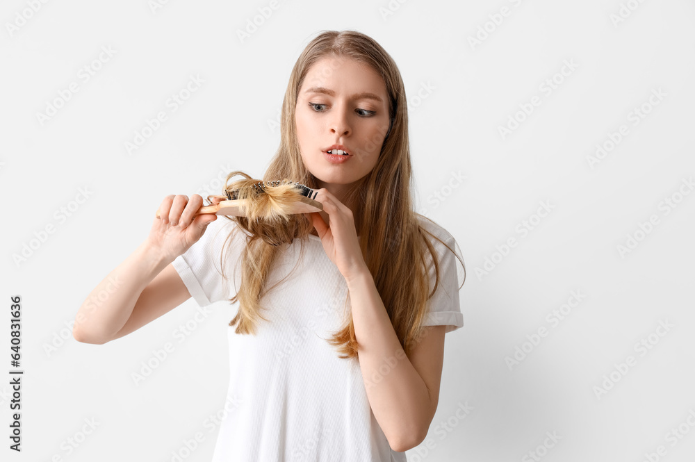 Young woman with hair loss problem brushing on light background