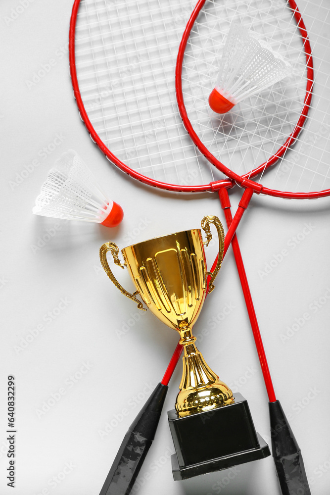 Gold cup with badminton rackets and shuttlecocks on light background