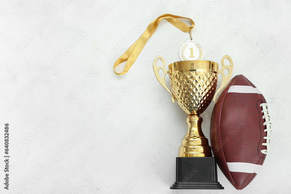 Gold cup with first place medal and rugby ball on white background