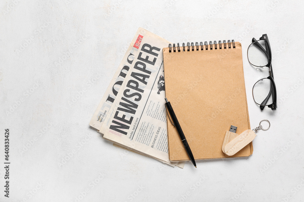 Notebook with USB flash drive, newspapers and eyeglasses on white background