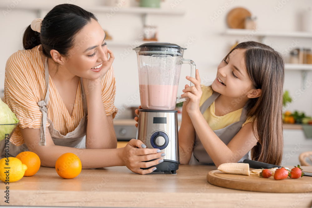 Little girl and her mother making smoothie with blender in kitchen