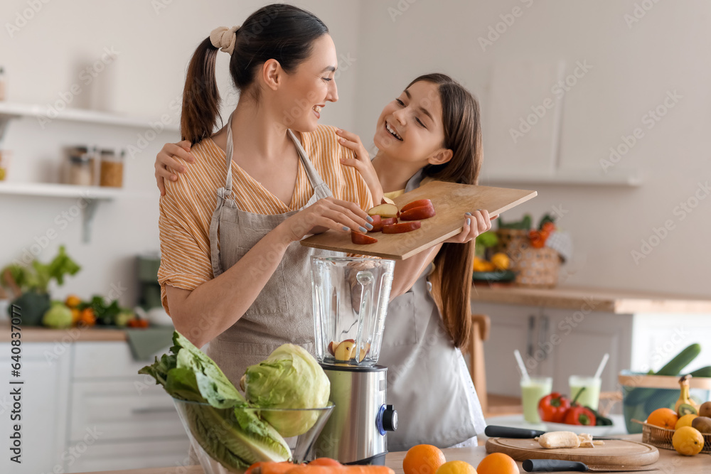 Little girl with her mother putting cut apple into blender in kitchen