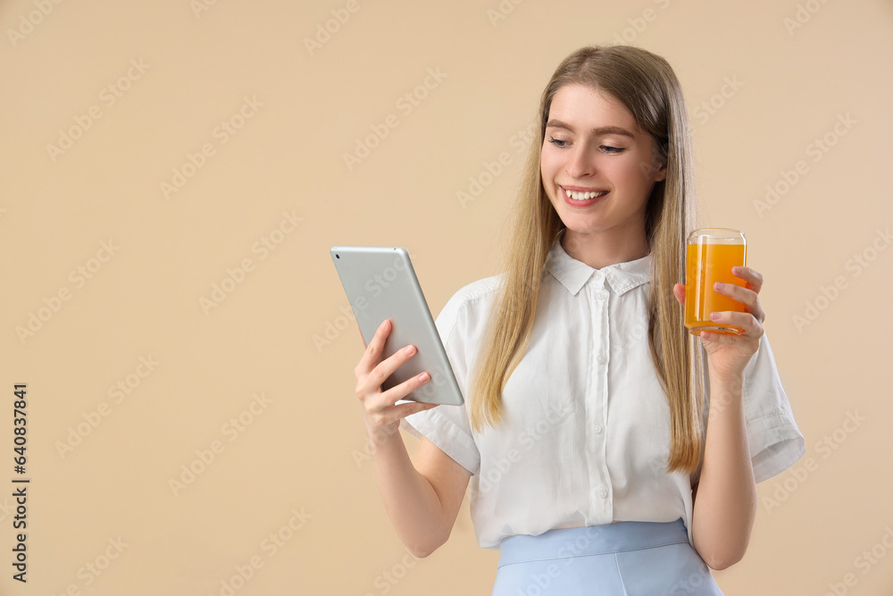 Young woman with glass of vegetable juice and tablet computer on beige background