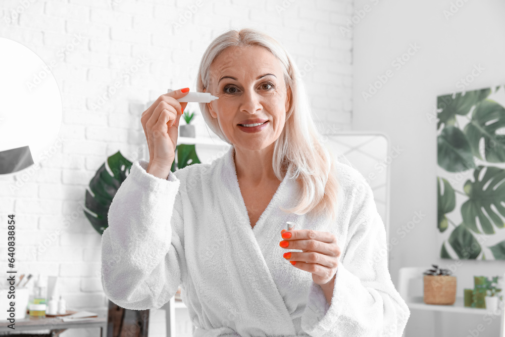 Mature woman applying under-eye cream in bathroom