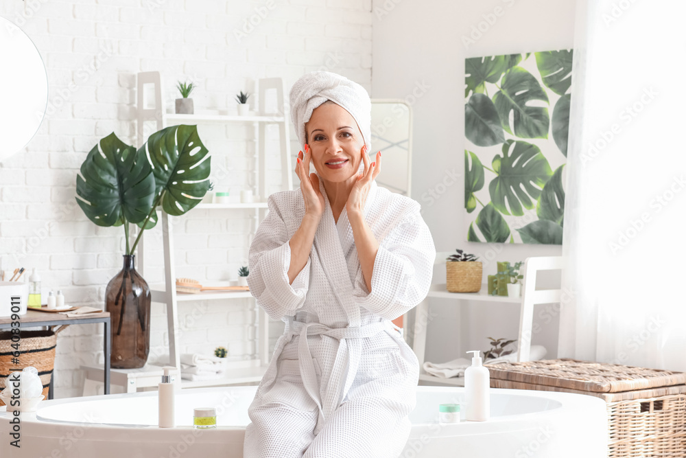 Mature woman applying facial cream in bathroom