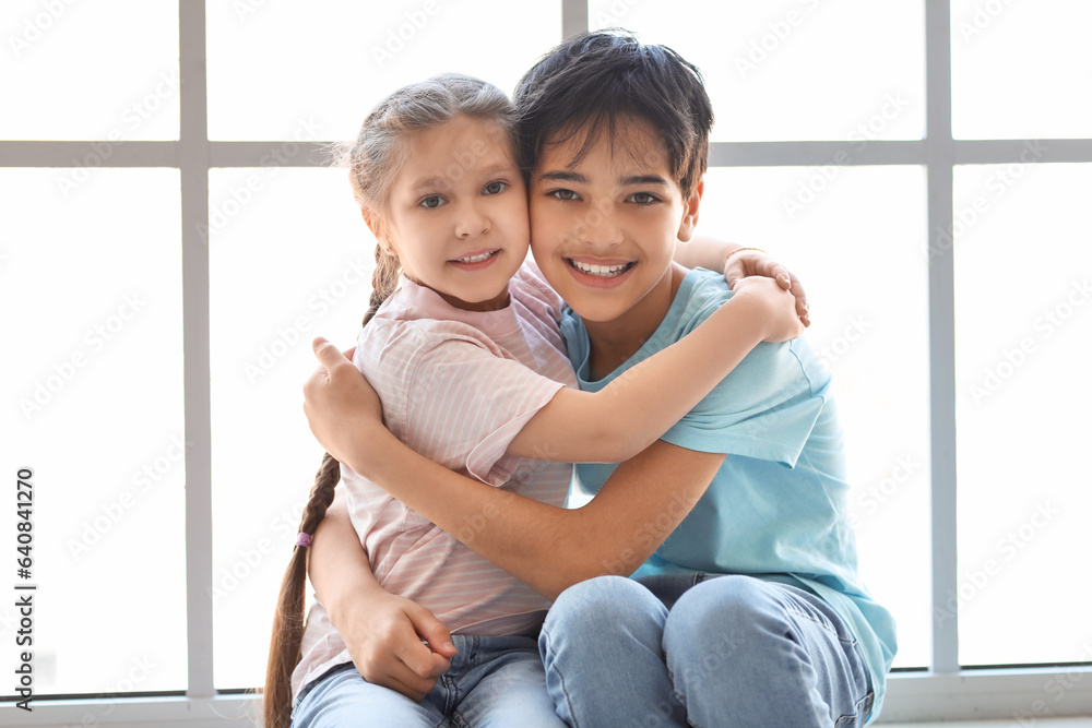 Little boy with his sister hugging near window