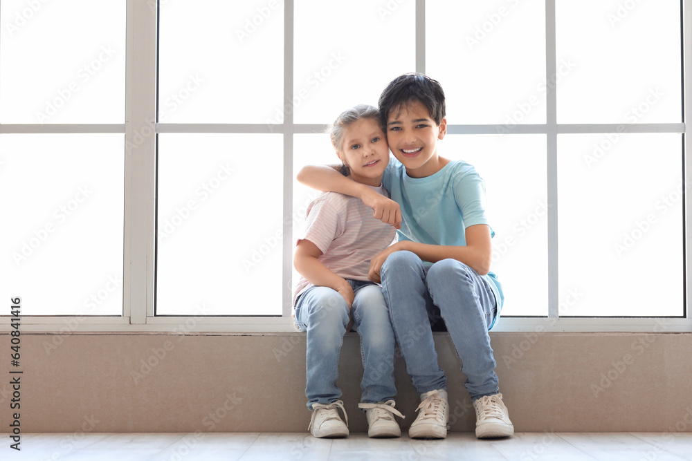 Little boy with his sister hugging near window