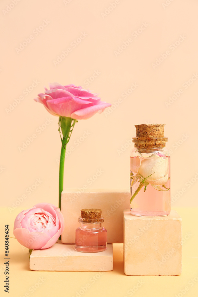 Bottles of cosmetic oil with rose extract and flowers on beige background