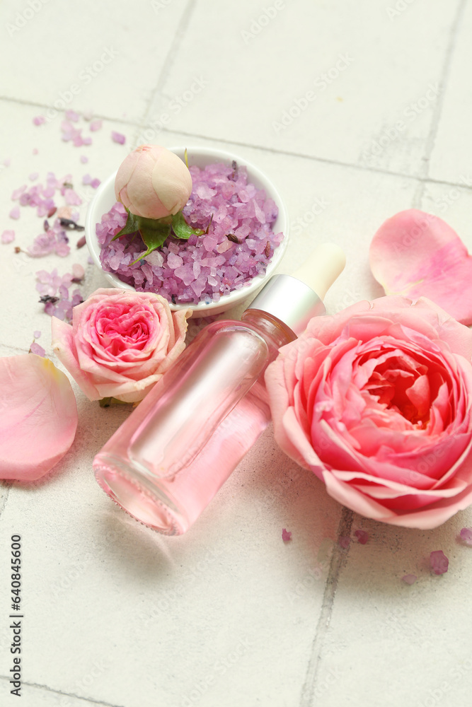 Bottle of cosmetic oil with rose extract and flowers on white tile background