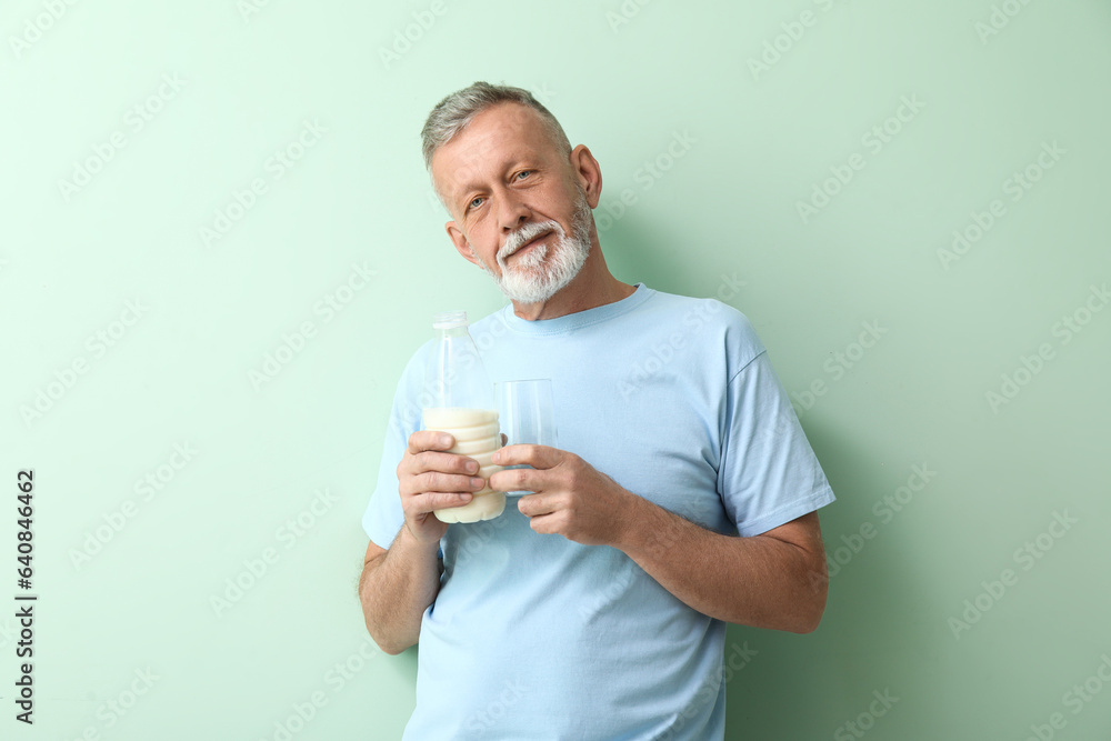 Mature man with bottle and glass of milk on green background