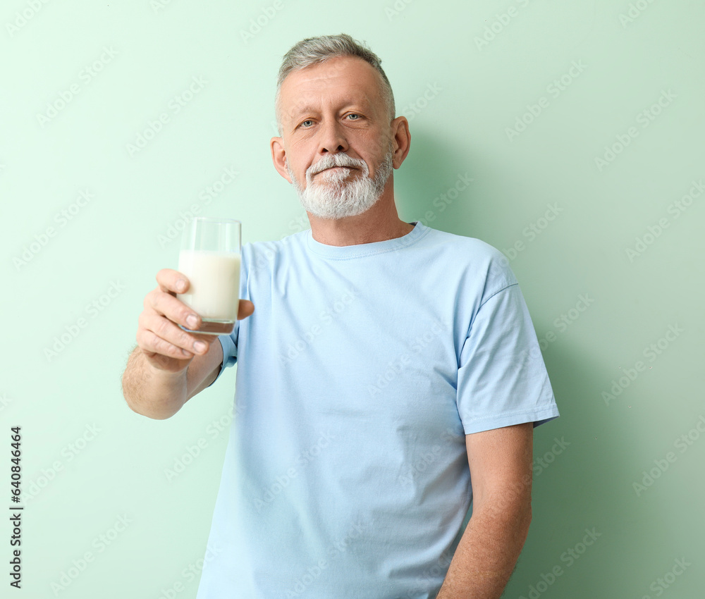 Mature man with glass of milk on green background