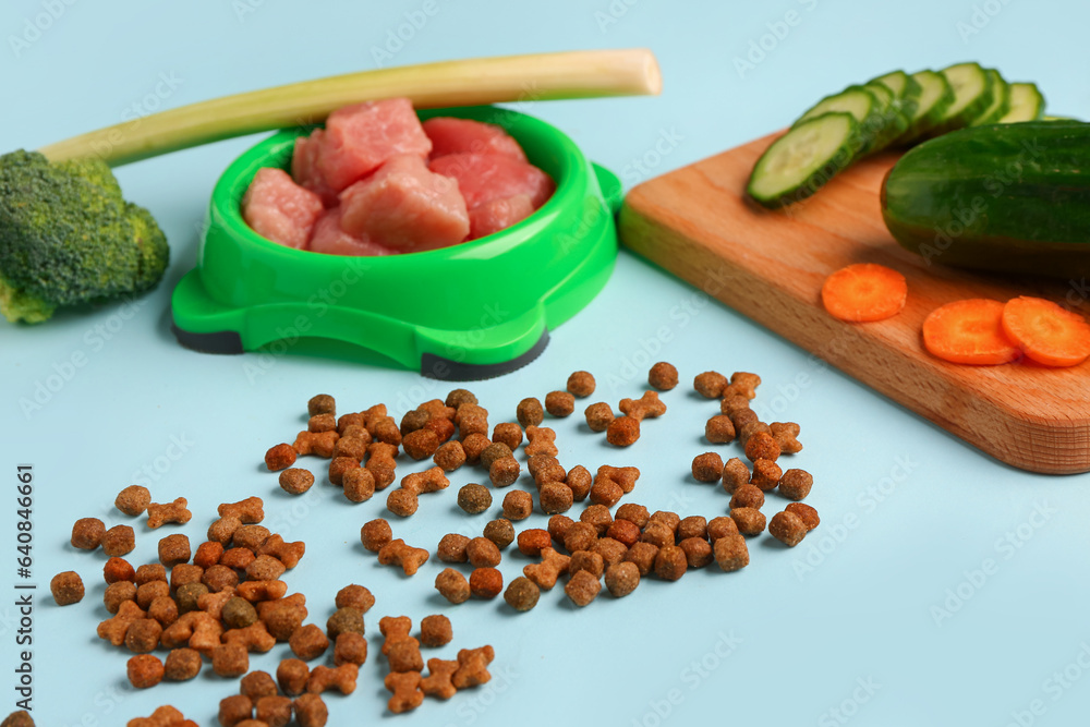 Dry pet food, raw meat and natural products on blue background