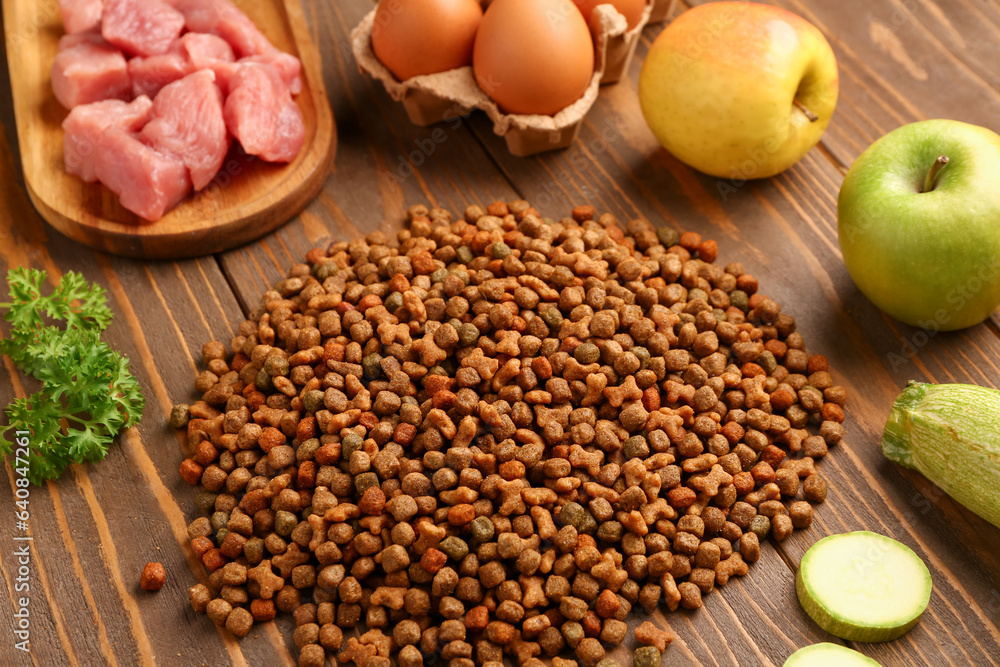 Dry pet food, raw meat and natural products on wooden background, closeup