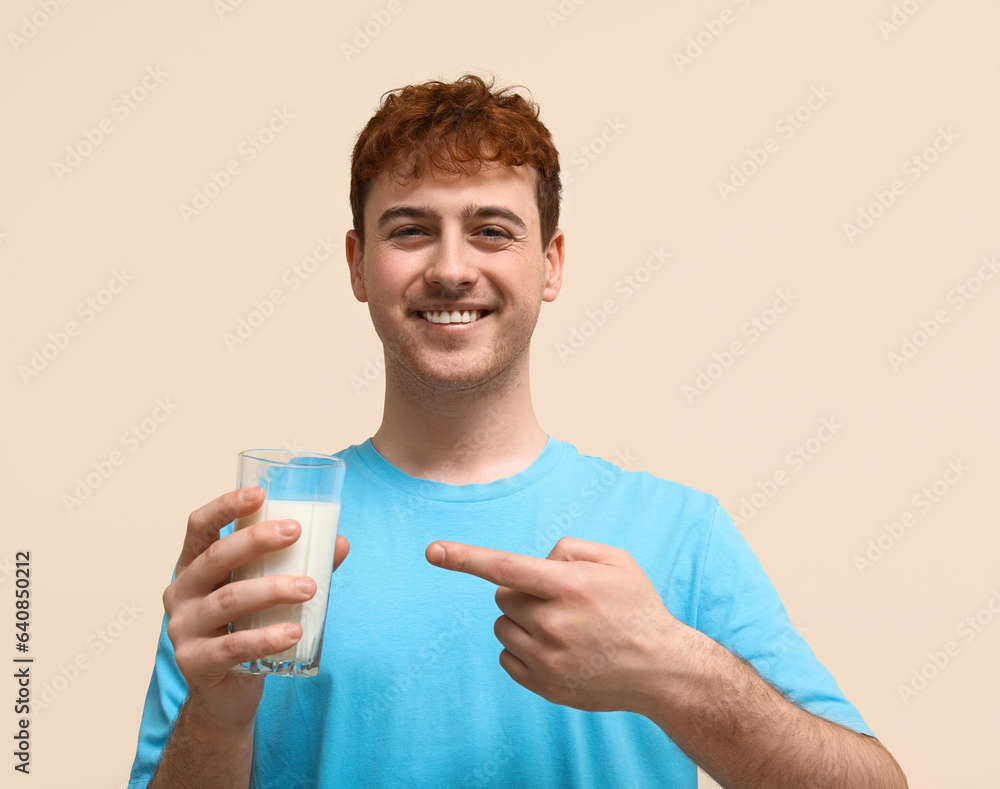 Young man pointing at glass of milk on beige background