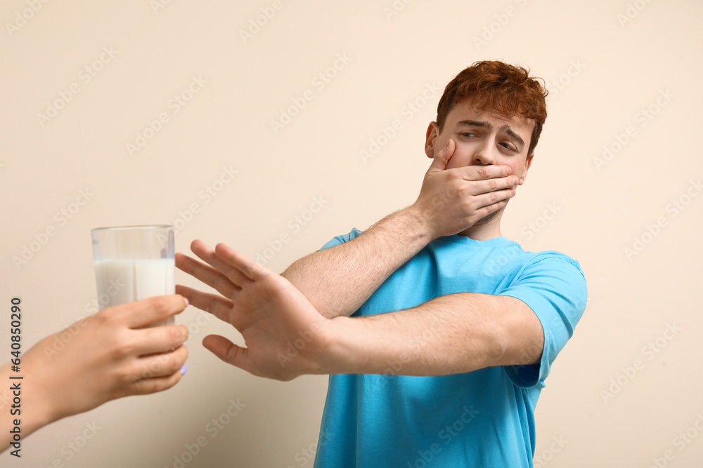 Displeased young man rejecting glass of milk on beige background