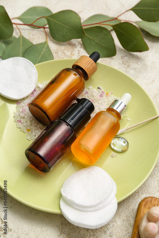 Plate with cosmetic products, cotton pads and sea salt on light background, closeup