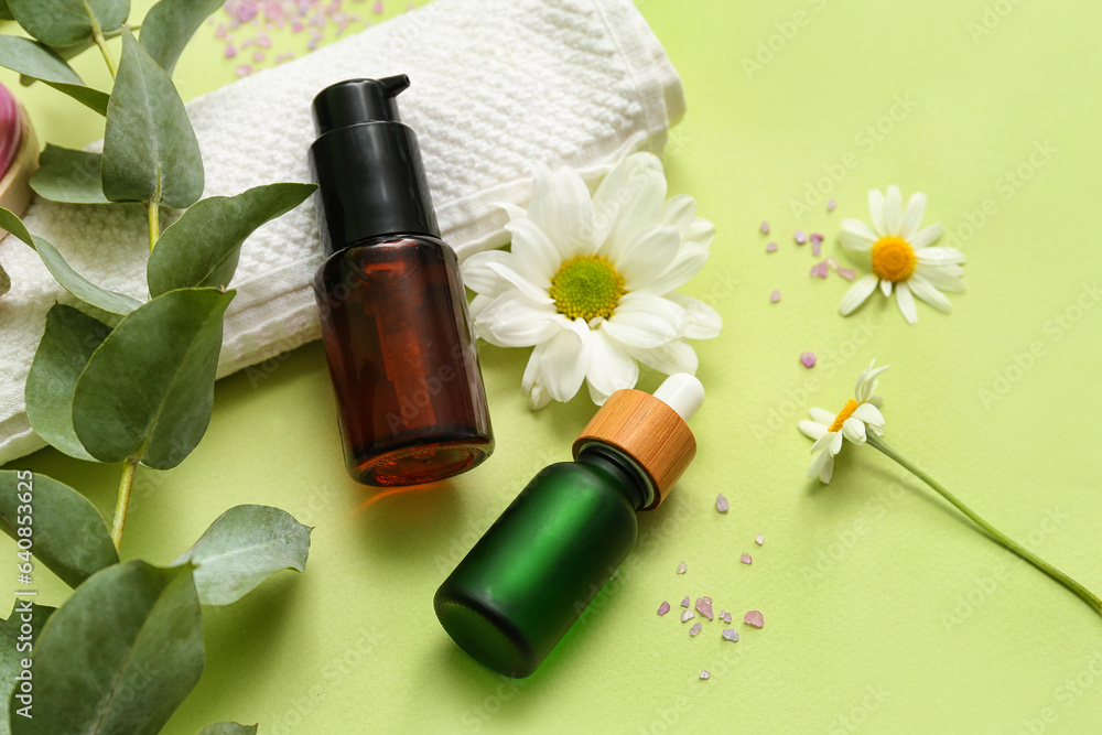 Composition with bottles of cosmetic products, clean towel and flowers on green background