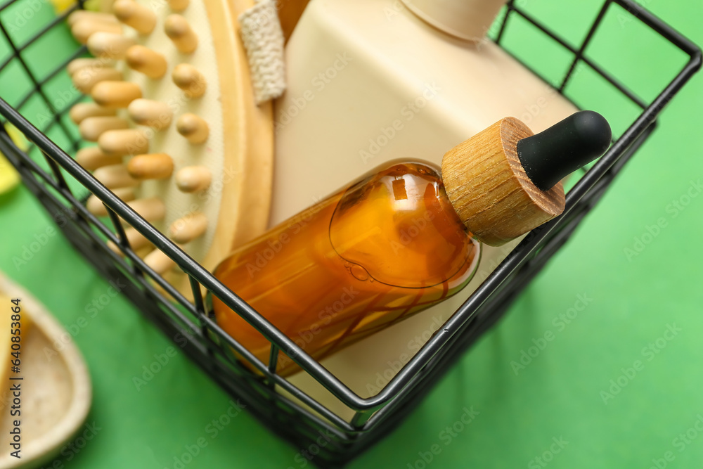 Basket with cosmetic products and massage brush on green background, closeup