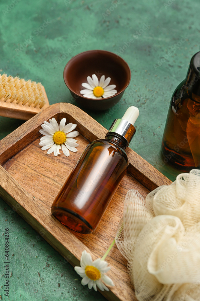 Wooden board with bottle of essential oil, bath supplies and chamomile flowers on color background, 