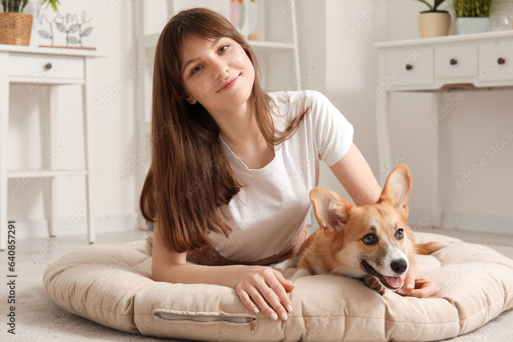 Pretty young woman lying on pet bed with cute Corgi dog in living room