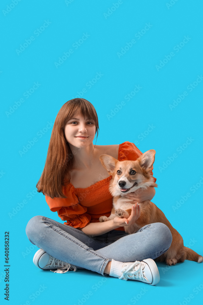 Pretty young woman sitting with cute Corgi dog on blue background