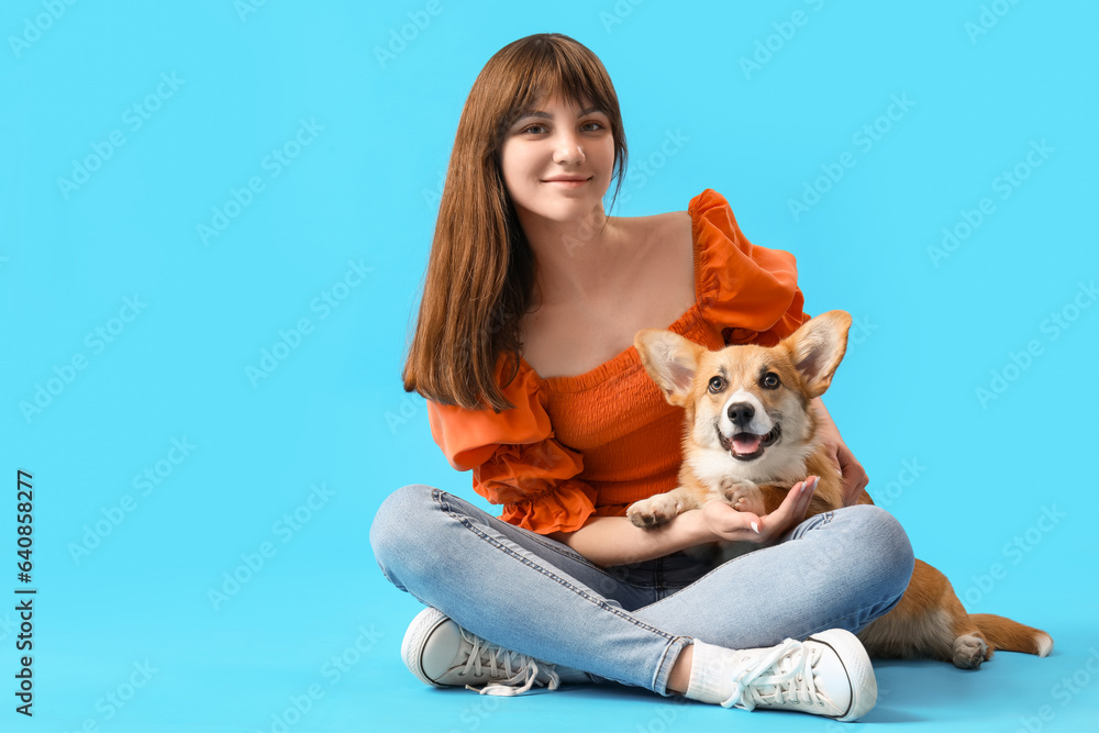 Pretty young woman sitting with cute Corgi dog on blue background