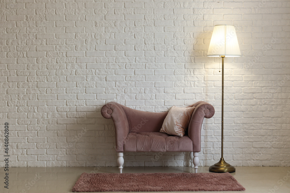 Glowing lamp with armchair near white brick wall in room