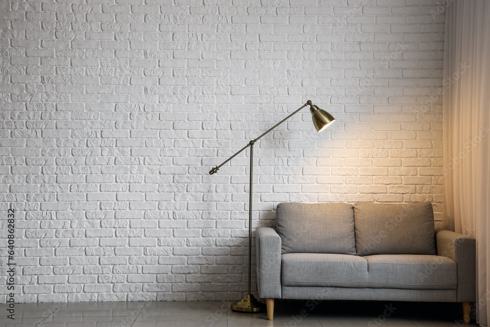 Glowing lamp with sofa near white brick wall in room