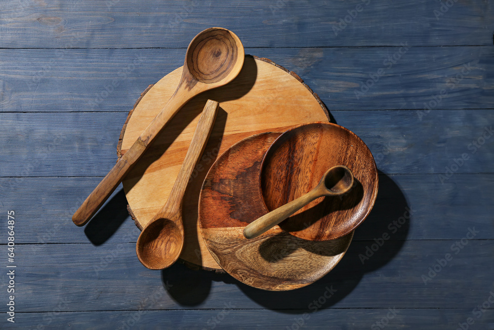 New cutting board, plates and spoons on blue wooden background