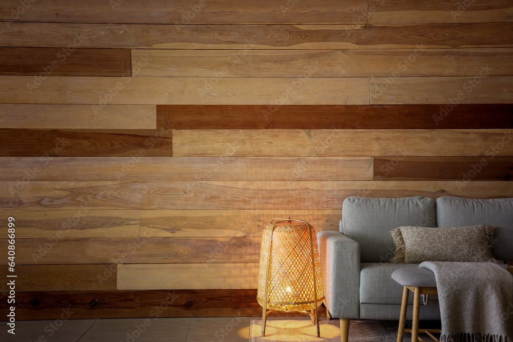 Glowing lamp, grey sofa and bench near wooden wall