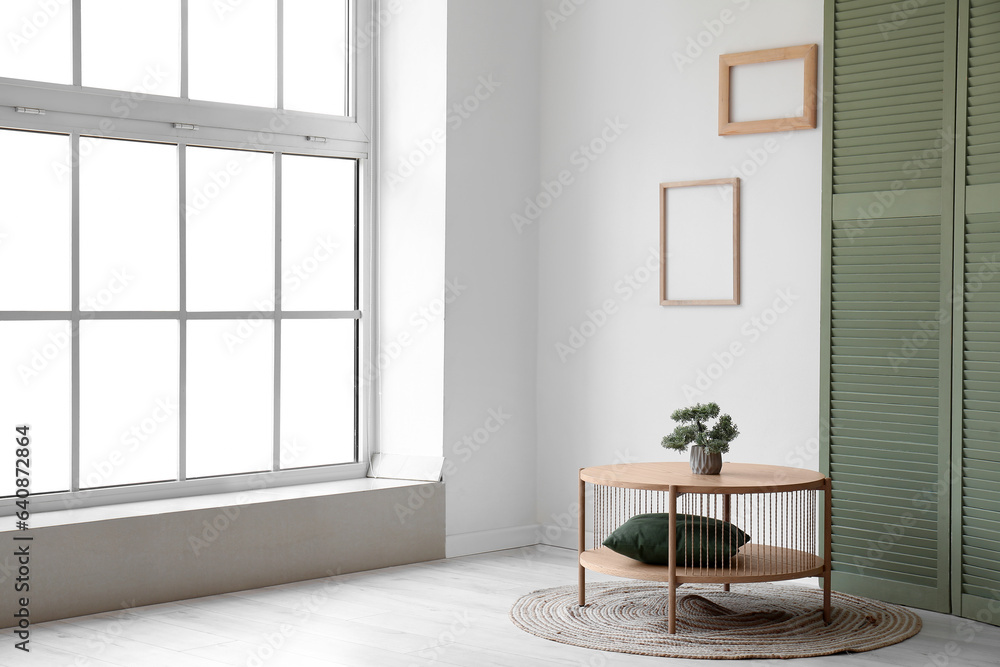 Wooden coffee table with bonsai tree and green folding screen near window