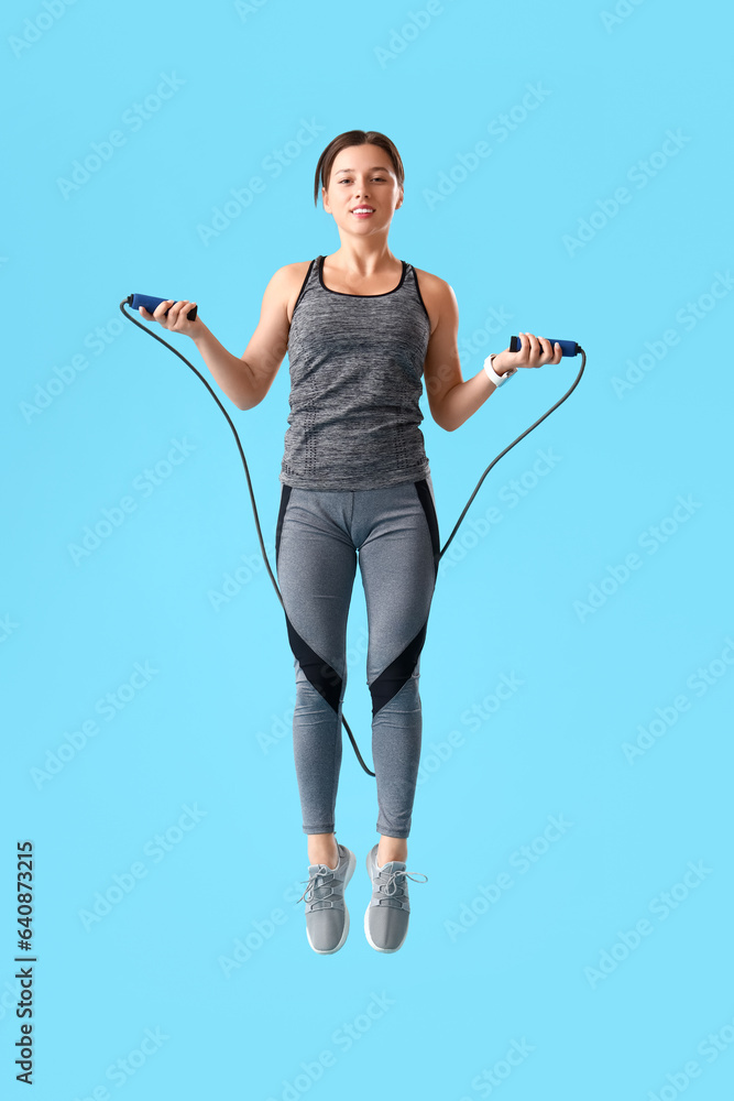 Sporty young woman jumping rope on blue background