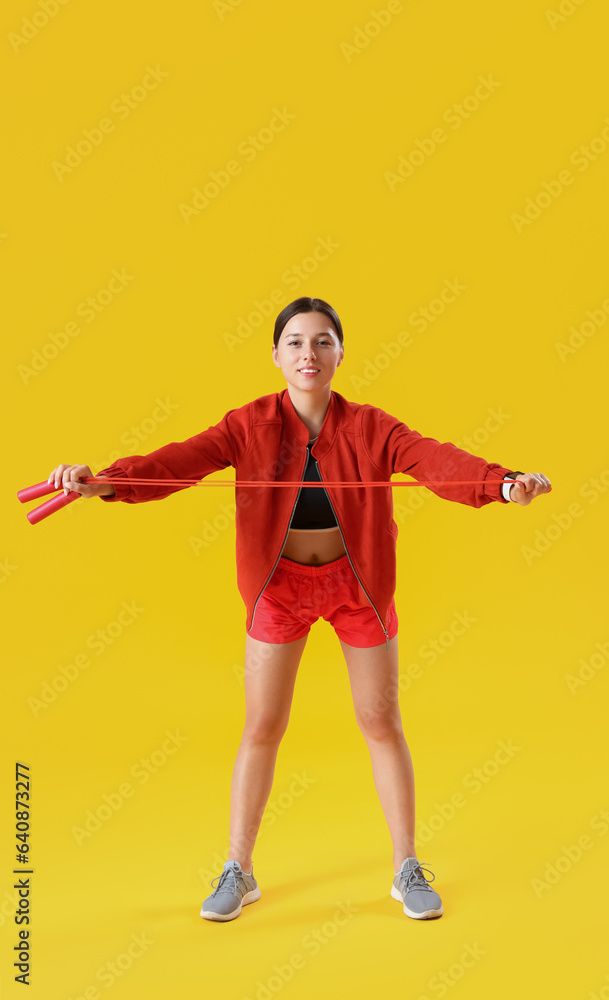 Sporty young woman training with jumping rope on yellow background